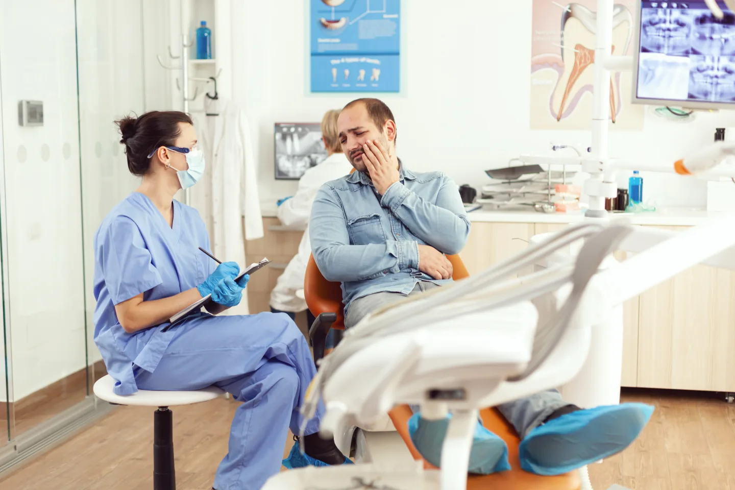 Ein Patient hält sich im Gespräch mit einer Mitarbeiterin der Zahnarztpraxis die Wange.