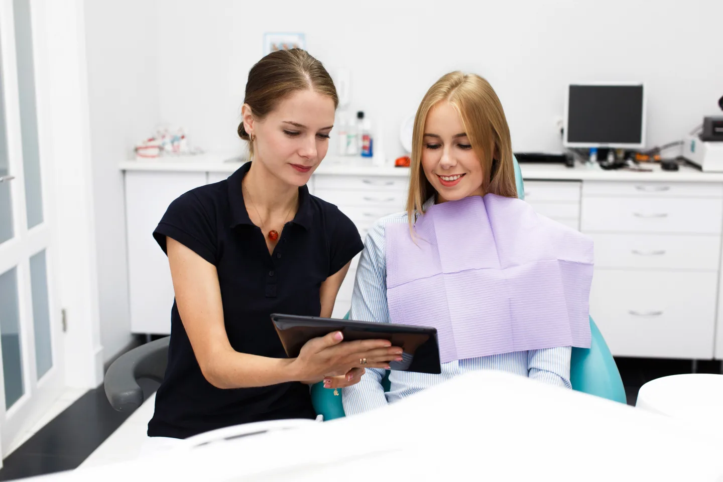 Zwei Frauen betrachten gemeinsam ein Tablet im zahnärztlichen Behandlungsraum.