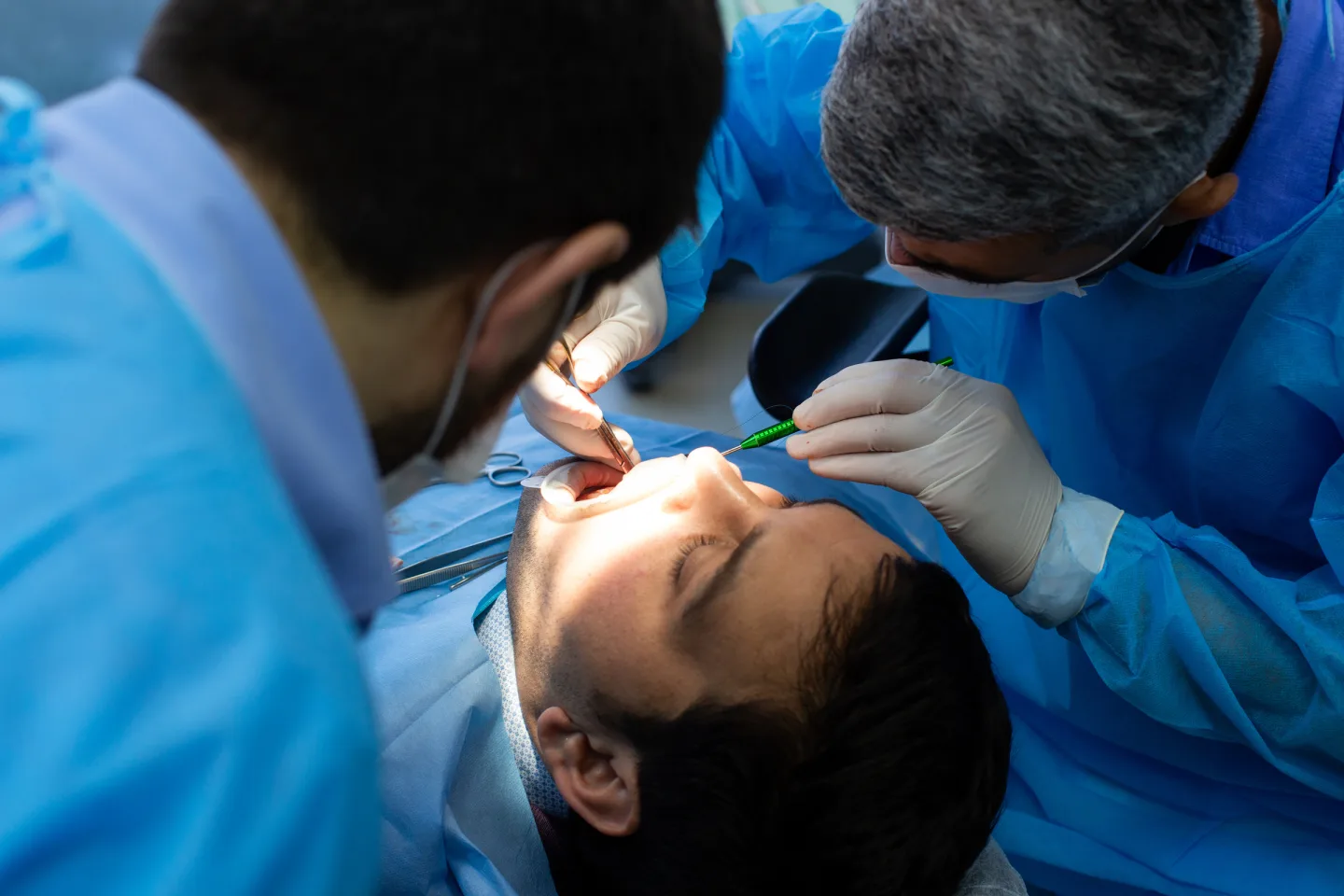 Zahnarzt und Assistent betreuen einen Patienten während eines zahnärztlichen Eingriffs.