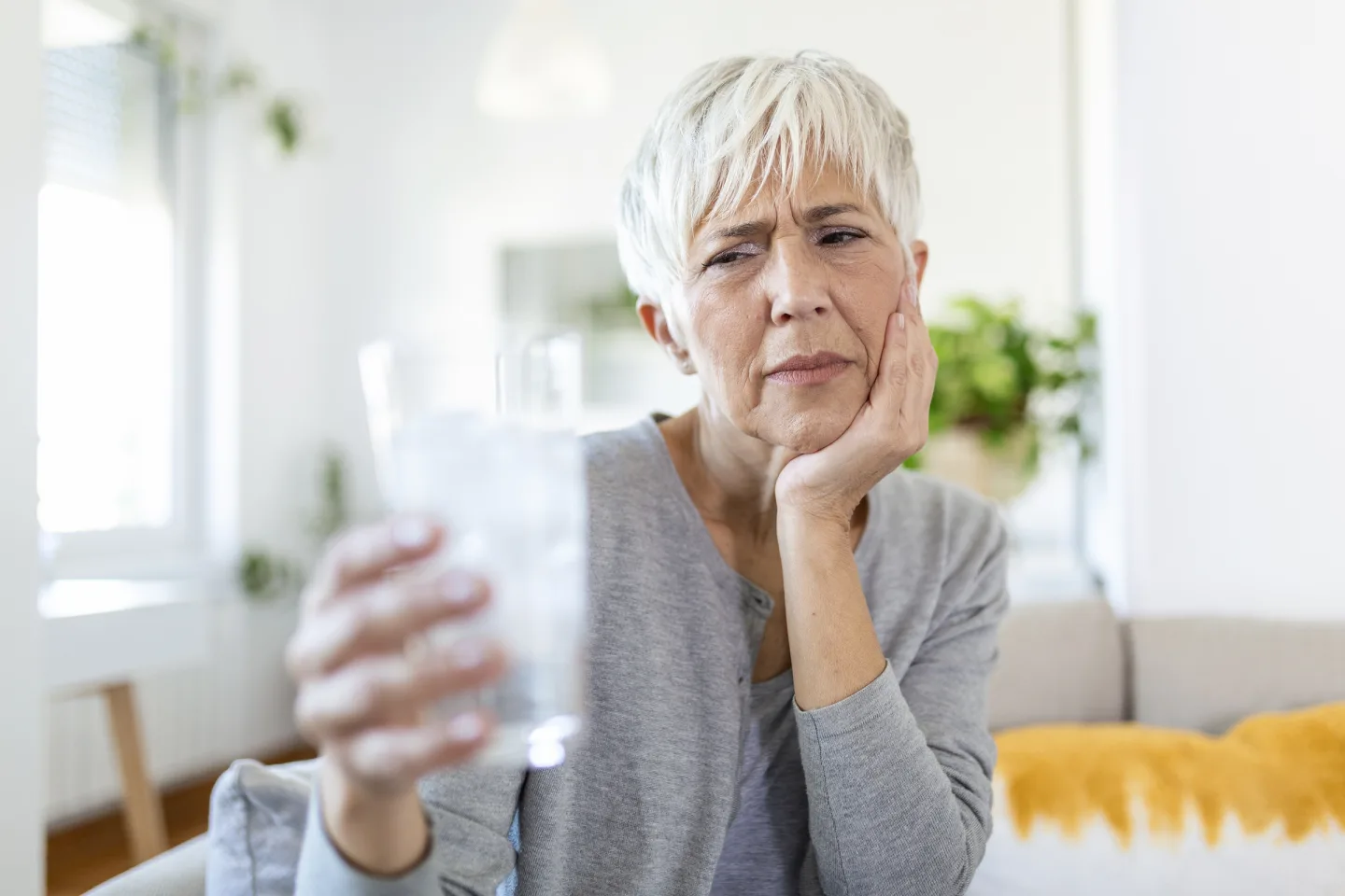 Woman with tooth discomfort holding cold water.