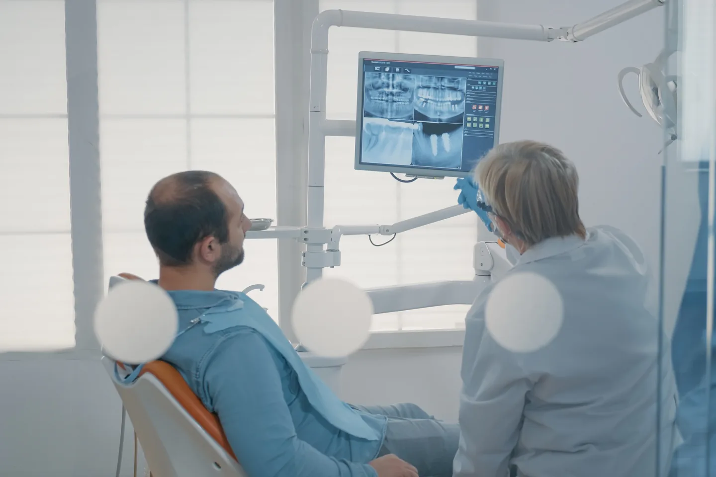 Zahnmedizinische Fachkraft zeigt einem Patienten ein Röntgenbild auf einem Bildschirm.